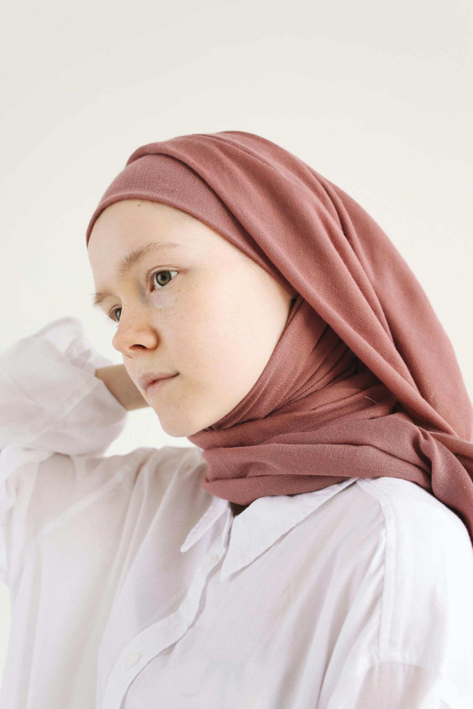 A young woman wearing a hijab, posing in a soft light. Perfect for lifestyle or cultural themes.